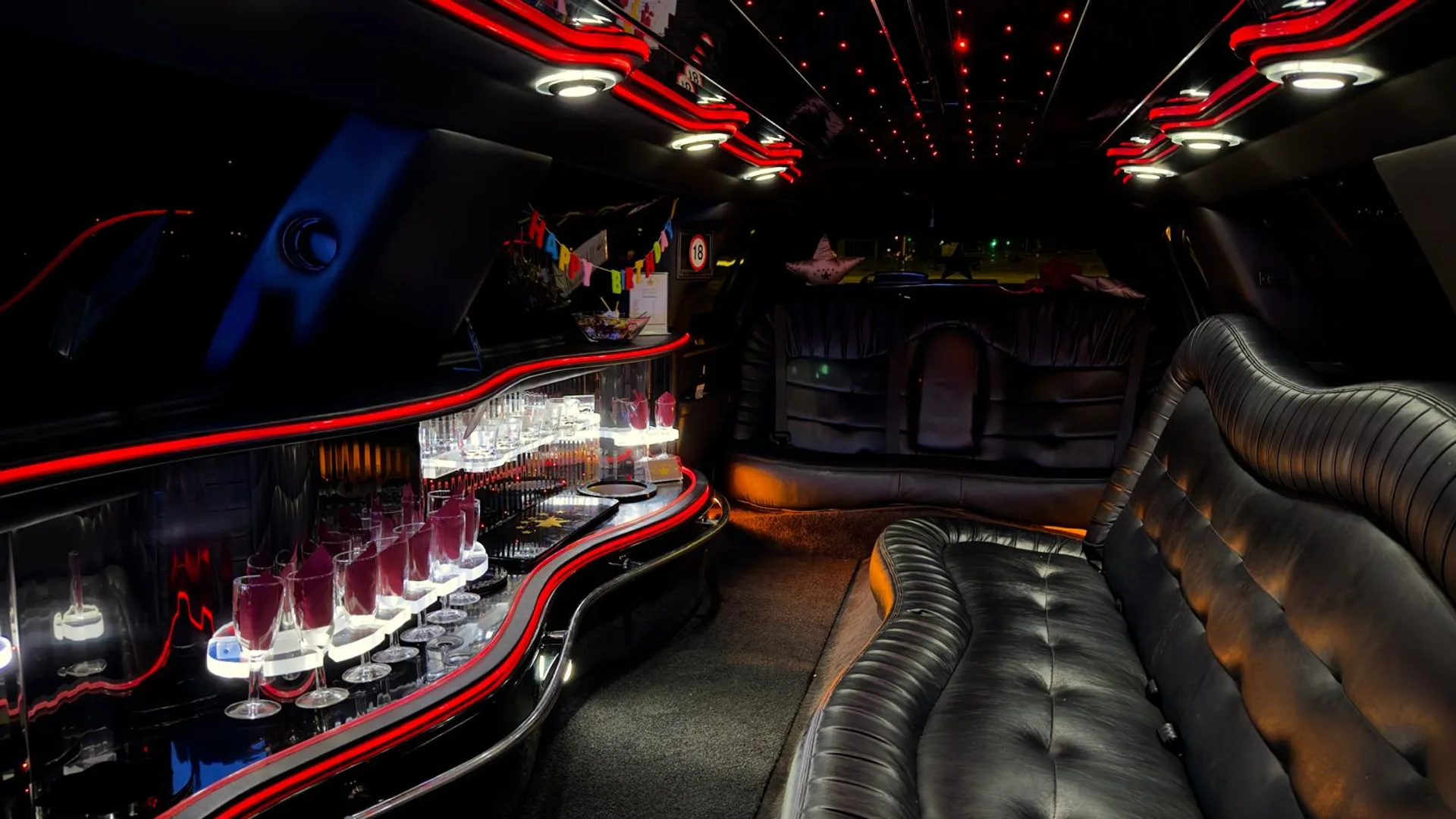 Partylimousine Bar & Bühne Wien | MrRa Partylimousine Innenraum mit Sektgläsern, Bar und roter LED-Beleuchtung.